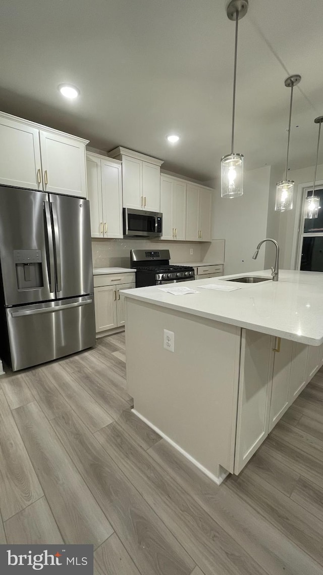 kitchen with appliances with stainless steel finishes, sink, decorative light fixtures, a center island with sink, and white cabinetry