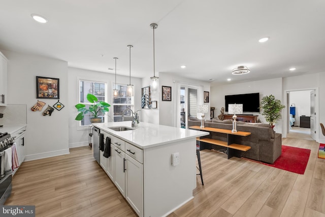 kitchen featuring white cabinets, sink, hanging light fixtures, an island with sink, and a breakfast bar area