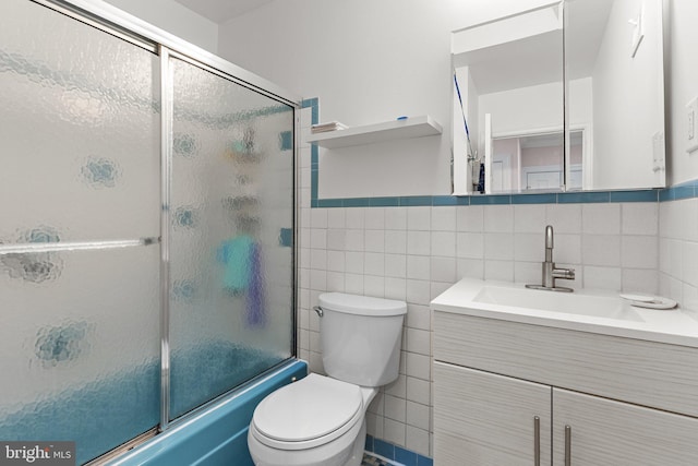 full bathroom with shower / bath combination with glass door, vanity, toilet, and tile walls