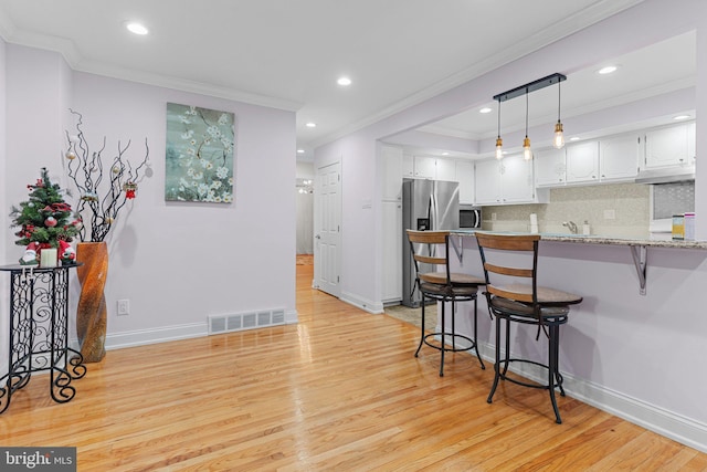 kitchen with white cabinets, appliances with stainless steel finishes, light hardwood / wood-style floors, kitchen peninsula, and a breakfast bar area