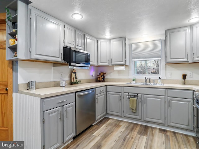 kitchen with gray cabinetry, sink, light hardwood / wood-style floors, a textured ceiling, and appliances with stainless steel finishes