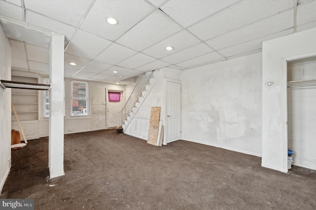 basement featuring a paneled ceiling and dark colored carpet