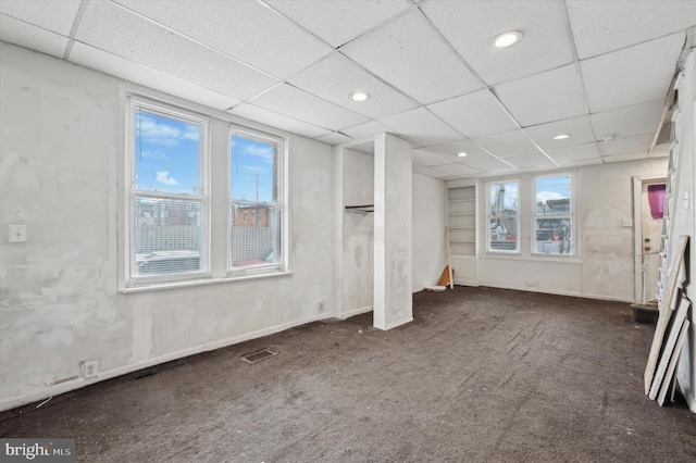 carpeted empty room featuring a drop ceiling and a healthy amount of sunlight