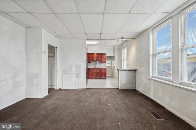 unfurnished living room featuring dark colored carpet, a paneled ceiling, and a healthy amount of sunlight