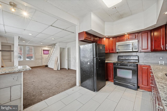 kitchen featuring black appliances, light colored carpet, and light stone counters