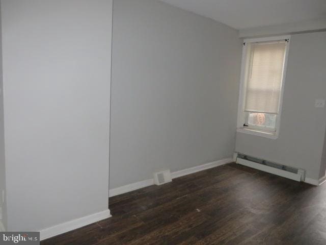 empty room featuring dark wood-type flooring and a baseboard radiator