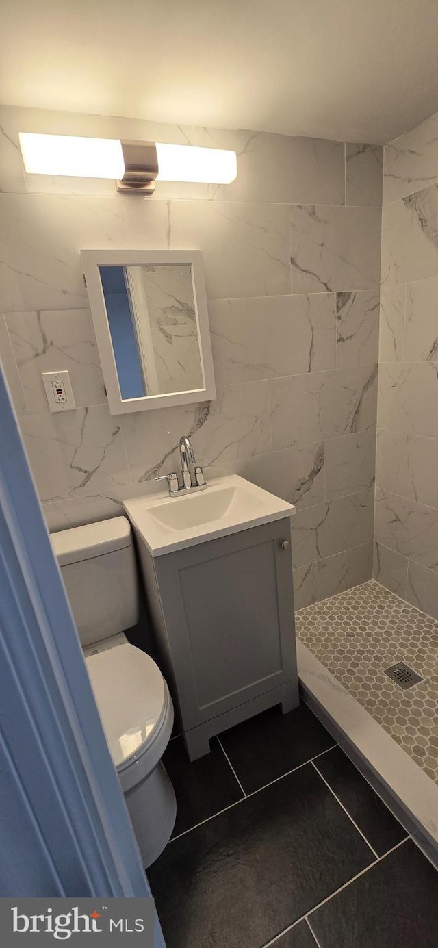 bathroom with toilet, tile patterned flooring, tile walls, and tiled shower