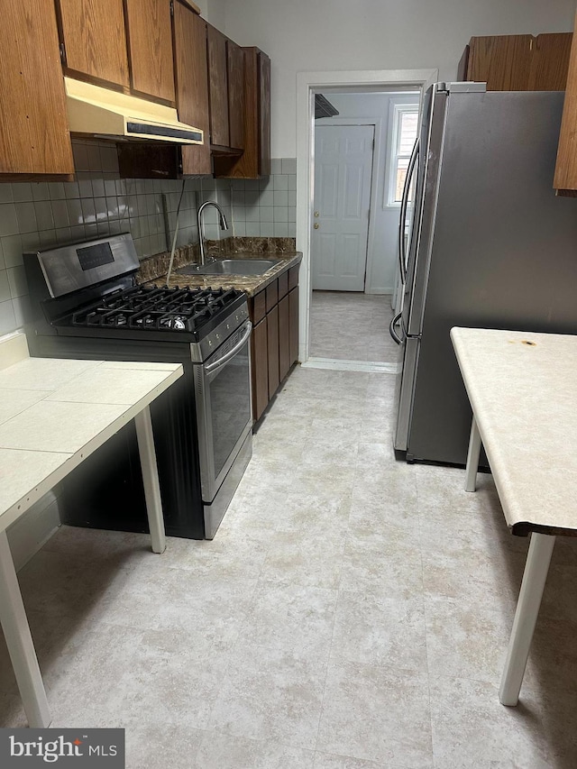 kitchen with stainless steel appliances, decorative backsplash, a sink, and under cabinet range hood