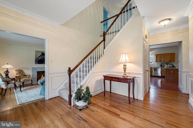 stairway with wood-type flooring, ornamental molding, and a premium fireplace