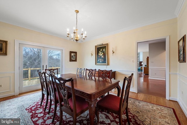 dining space with hardwood / wood-style flooring, french doors, ornamental molding, and a notable chandelier