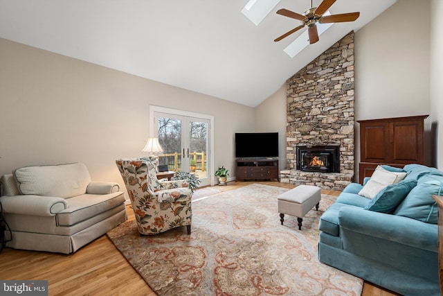 living room with ceiling fan, wood-type flooring, a skylight, a stone fireplace, and high vaulted ceiling