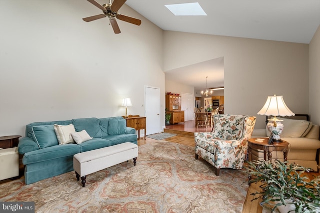 living room with a skylight, light hardwood / wood-style floors, ceiling fan with notable chandelier, and high vaulted ceiling