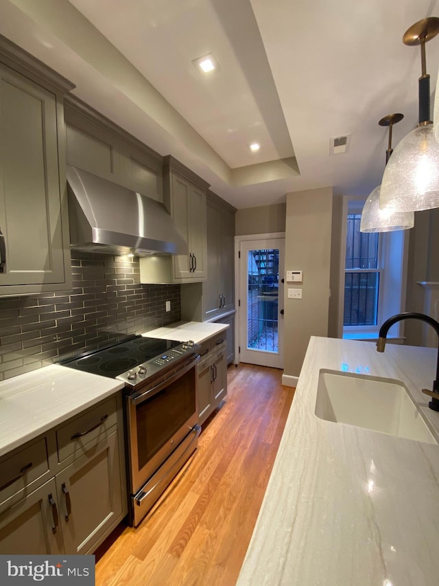 kitchen featuring wall chimney range hood, sink, stainless steel stove, decorative light fixtures, and light hardwood / wood-style floors