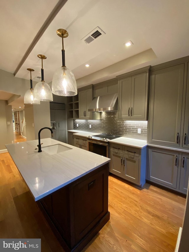 kitchen featuring sink, exhaust hood, decorative light fixtures, and light wood-type flooring