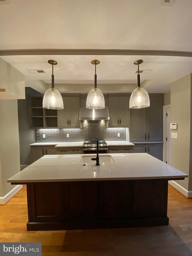 kitchen with backsplash, a kitchen island with sink, and hardwood / wood-style flooring