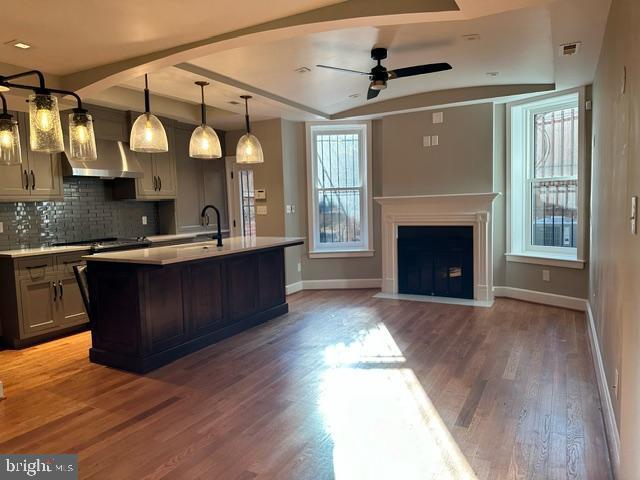 kitchen featuring pendant lighting, a kitchen island with sink, ceiling fan, beamed ceiling, and wood-type flooring