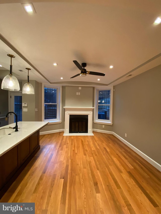 unfurnished living room featuring light hardwood / wood-style floors, ceiling fan, and sink