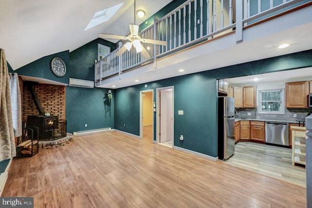 living room with a wood stove, high vaulted ceiling, a skylight, light wood-type flooring, and a wall unit AC