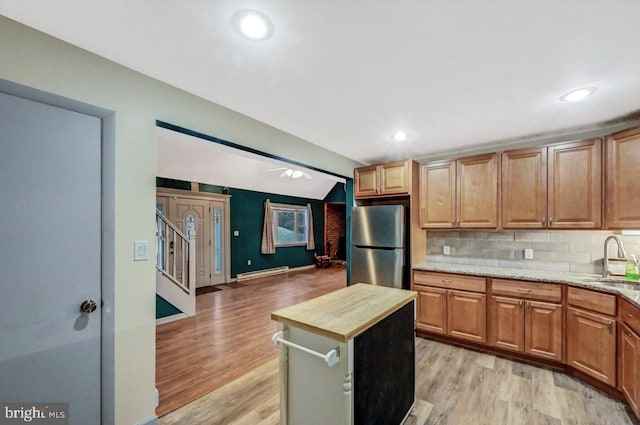 kitchen featuring light stone countertops, sink, baseboard heating, stainless steel fridge, and light wood-type flooring