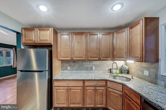 kitchen featuring sink, stainless steel appliances, tasteful backsplash, light stone counters, and light hardwood / wood-style flooring