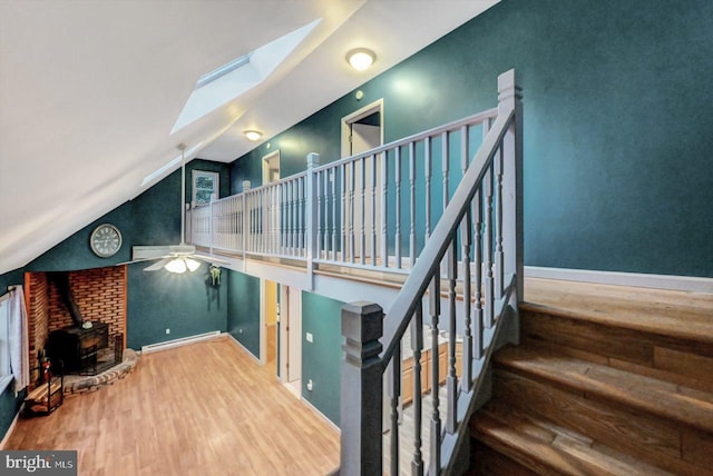 stairway featuring vaulted ceiling with skylight, ceiling fan, baseboard heating, hardwood / wood-style flooring, and a wood stove