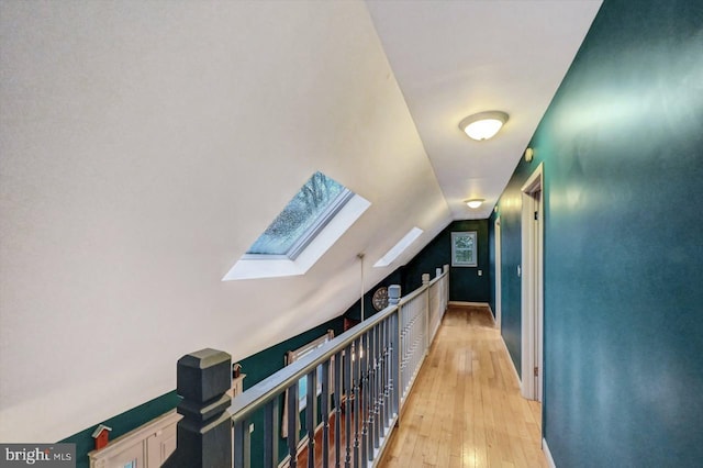 hallway featuring lofted ceiling with skylight and light wood-type flooring