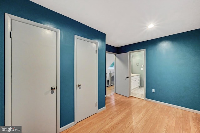 unfurnished bedroom featuring ensuite bathroom and light hardwood / wood-style flooring