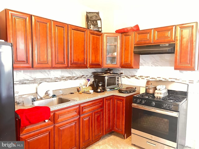 kitchen with black refrigerator, tasteful backsplash, sink, light tile patterned floors, and stainless steel gas range