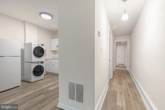 laundry room with cabinets, light wood-type flooring, sink, and stacked washer and clothes dryer