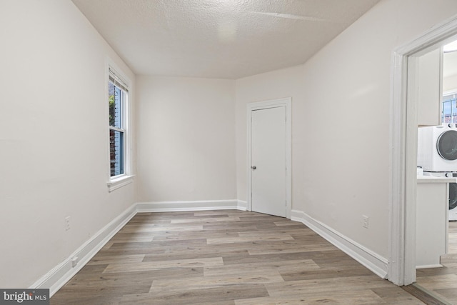 empty room featuring a textured ceiling, light hardwood / wood-style floors, and stacked washer / drying machine