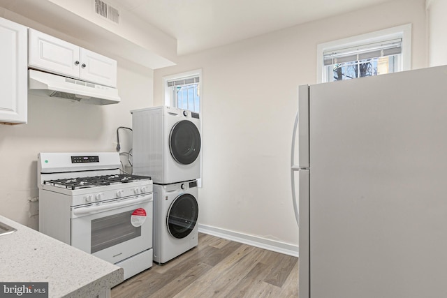 kitchen with a healthy amount of sunlight, white appliances, stacked washer and dryer, and light hardwood / wood-style flooring