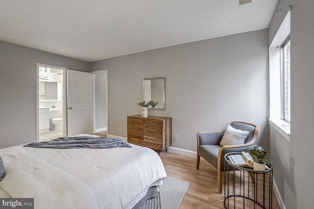 bedroom featuring connected bathroom, multiple windows, and light hardwood / wood-style flooring