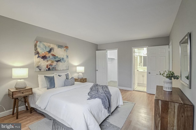 bedroom with a closet, ensuite bath, a spacious closet, and light hardwood / wood-style flooring