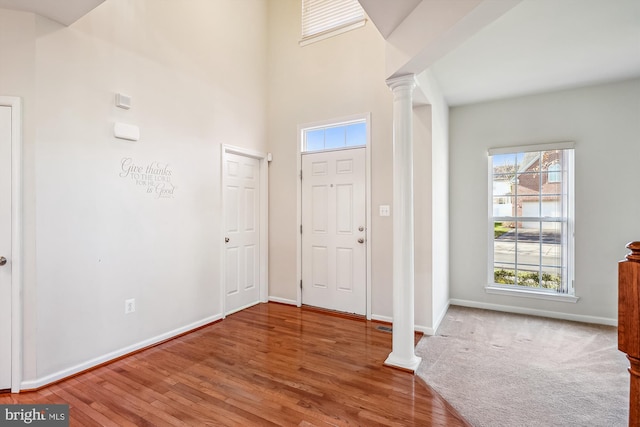 foyer entrance with ornate columns, hardwood / wood-style floors, and a high ceiling