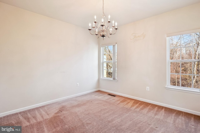 spare room featuring carpet flooring, a chandelier, and a healthy amount of sunlight