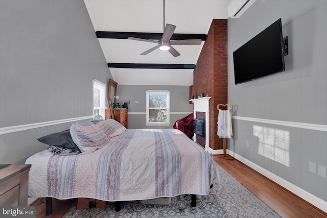 bedroom with a wall mounted air conditioner, hardwood / wood-style flooring, vaulted ceiling with beams, ceiling fan, and a large fireplace