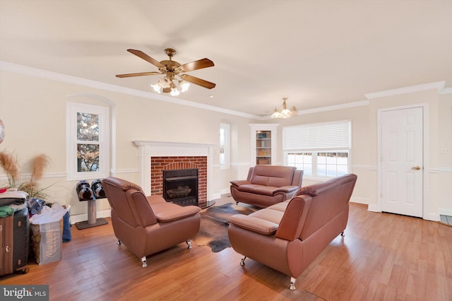 living room featuring a brick fireplace, crown molding, ceiling fan with notable chandelier, and light wood-type flooring