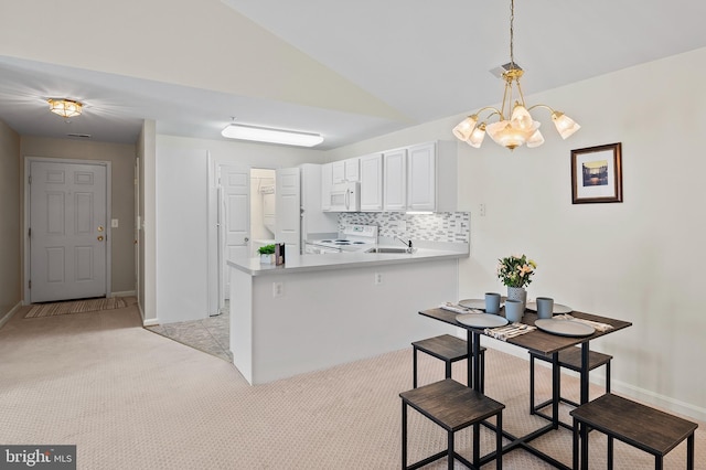 kitchen with kitchen peninsula, decorative backsplash, a kitchen breakfast bar, white appliances, and white cabinetry