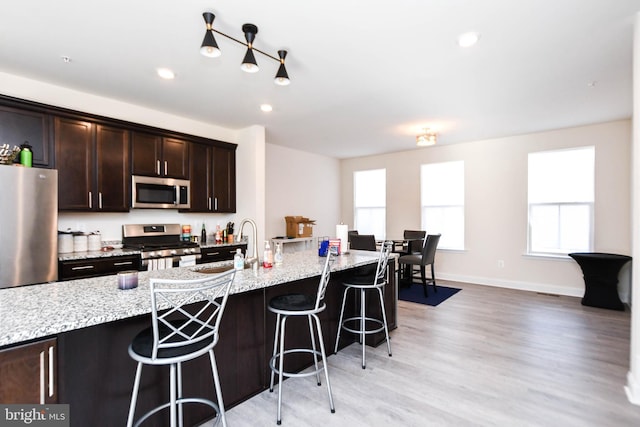 kitchen featuring light hardwood / wood-style floors, a kitchen breakfast bar, an island with sink, stainless steel appliances, and light stone counters