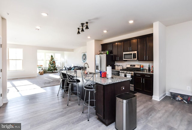 kitchen featuring a kitchen bar, stainless steel appliances, an island with sink, light wood-type flooring, and dark brown cabinets