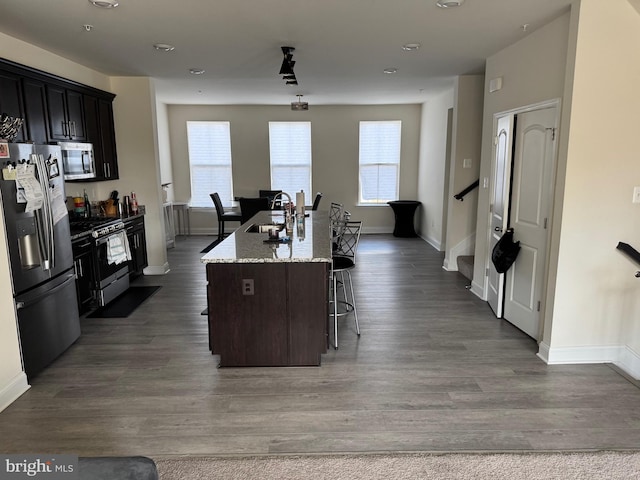 kitchen with sink, light stone counters, an island with sink, a breakfast bar area, and stainless steel appliances