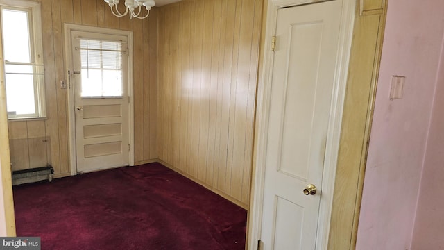 entryway with dark colored carpet, wooden walls, and a chandelier