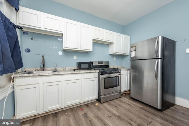 kitchen with hardwood / wood-style floors, sink, light stone countertops, white cabinetry, and stainless steel appliances