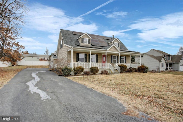 cape cod home with aphalt driveway, a porch, a front lawn, and roof mounted solar panels