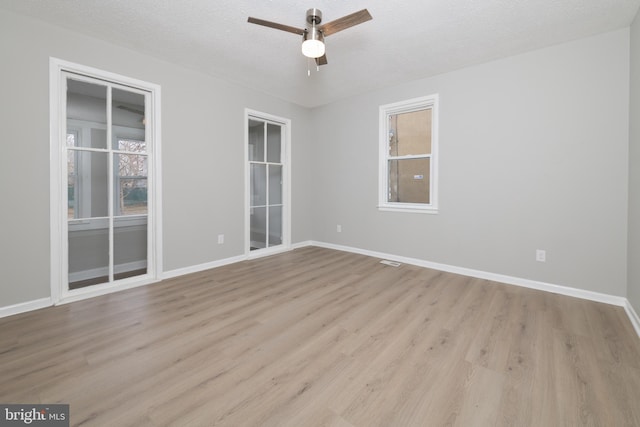 unfurnished room with a wealth of natural light, ceiling fan, light hardwood / wood-style floors, and a textured ceiling