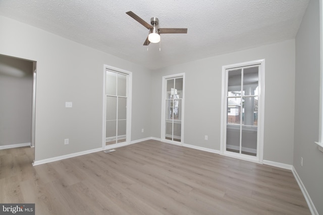 unfurnished room with a textured ceiling, light wood-type flooring, and ceiling fan