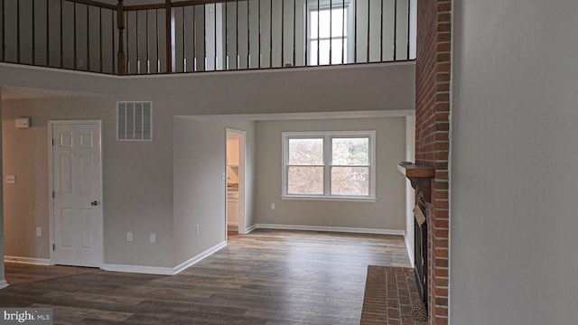 unfurnished living room with dark wood-type flooring, a high ceiling, and a brick fireplace