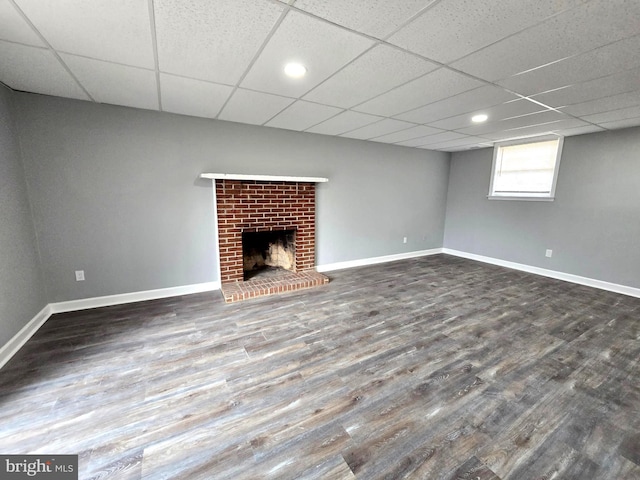 basement with a drop ceiling, dark wood-type flooring, and a brick fireplace