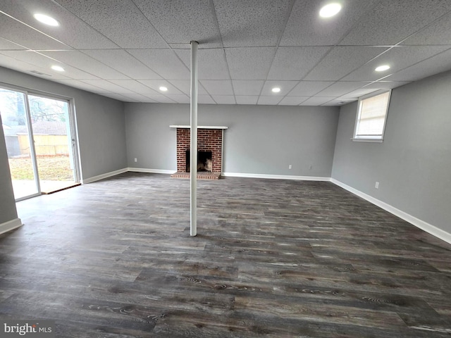 basement featuring a drop ceiling, dark hardwood / wood-style floors, a brick fireplace, and a wealth of natural light