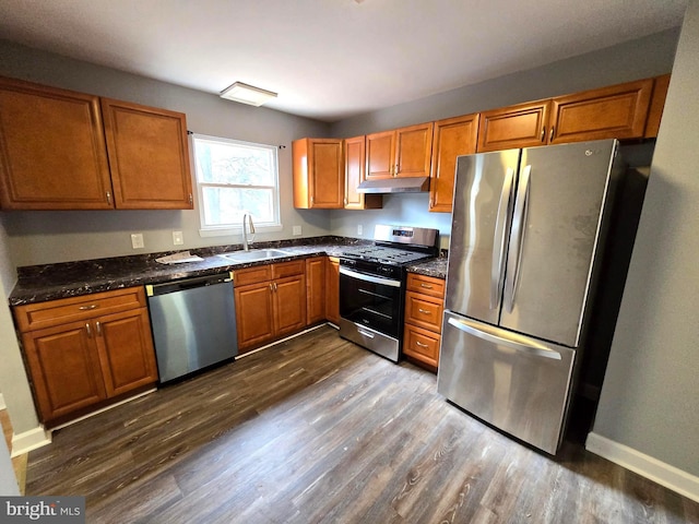 kitchen featuring dark hardwood / wood-style floors, sink, stainless steel appliances, and dark stone counters